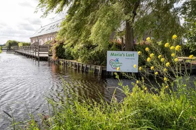 a sign next to a river with a building at Zaanse Rietveld Logies in Alphen aan den Rijn