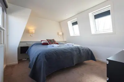 a bedroom with a bed with a blue blanket and two windows at Garden House Harry in Zandvoort