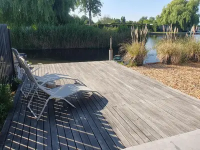 a bench sitting on a wooden deck next to a lake at Rustic Lake House in Vinkeveen