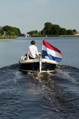 a man in a boat with a flag on the water at Lakehouses luxe family holiday house 6 pers in Oud-Ade