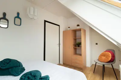 a white bedroom with a bed and a chair at Knus appartement met parkeerplek en zeezicht! in Egmond aan Zee