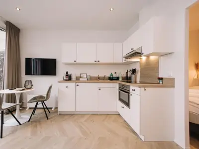 a kitchen with white cabinets and a table and a bed at Suite 55, near the beach in Zandvoort
