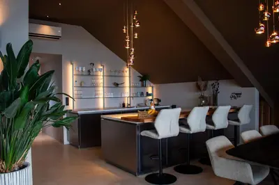 a kitchen with a bar with white stools at Enjoy Heaven in Schellinkhout