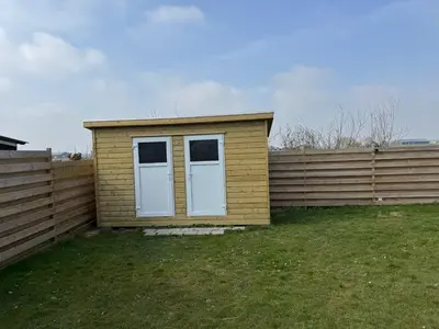 a small house with white doors next to a fence at Bungalowpark de Horn - 128 in Dirkshorn