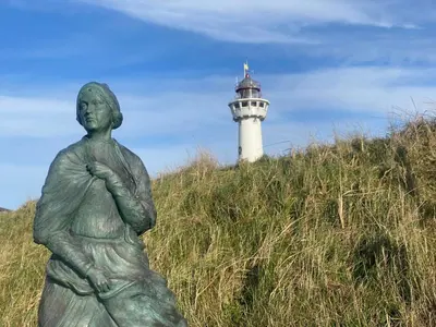 a statue of a woman with a lighthouse in the background at Kuifje aan Zee in Egmond aan Zee