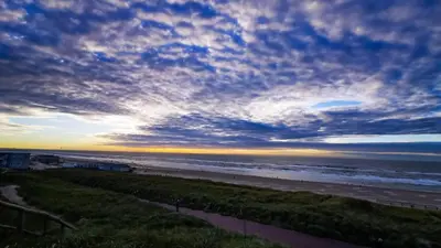 a view of a beach at sunset with the ocean at de Vuurtoren in Egmond aan Zee