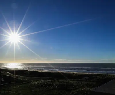 a sun shining over the ocean on a beach at de Vuurtoren in Egmond aan Zee