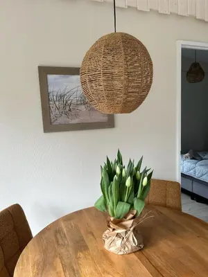 a round wooden table with a vase of flowers on it at Kings View Cottage, Helemaal vernieuwd 2025 in Warmenhuizen