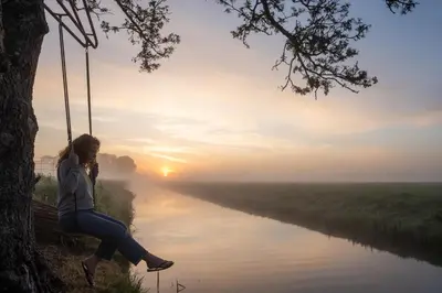 a woman sitting on a swing next to a river at Luxe Wikkelhouse met hottub 'Dompel' in Hoogwoud