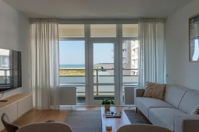 a living room with a couch and a large window at Lovina Beach House by Urban Home Stay in Egmond aan Zee