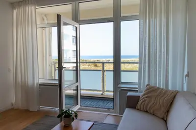 a living room with a couch and a large window at Lovina Beach House by Urban Home Stay in Egmond aan Zee