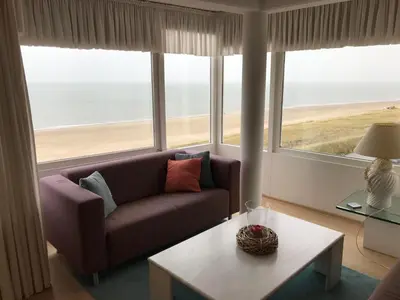 a living room with a couch and a table and windows at Zonnehoek 77 in Egmond aan Zee