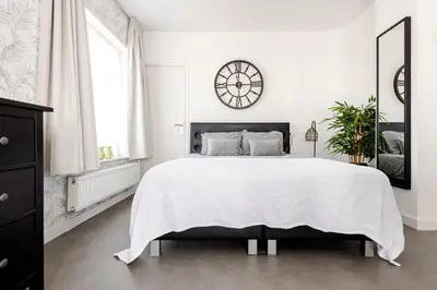 a white bedroom with a large bed and a clock on the wall at Beach and Dunes Studio - Free Parking in Zandvoort