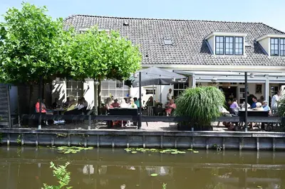 a group of people sitting at a restaurant next to a body of water at Abbey Abcoude in Abcoude