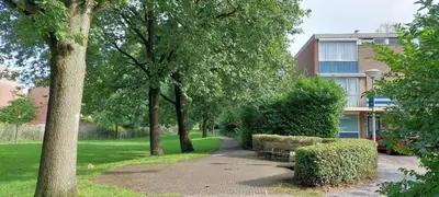a park with a bench and trees and a building at Hagerstudio in Huizen