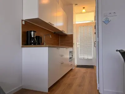 a kitchen with white cabinets and a wooden floor at Reumann Holiday Apartments De Schelp 12 in Zandvoort