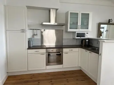 a white kitchen with white cabinets and a wooden floor at Appartement aan het water in Alkmaar