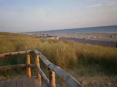 a wooden boardwalk leading to a beach with people on it at Pacific Ocean View Comfortable Holiday Residence in Bergen aan Zee