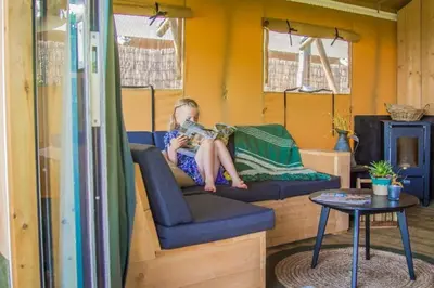 a young girl sitting on a couch in a tiny house at Zorgcamping De Ruif De Peppelhoeve in Stoutenburg