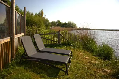 a chair sitting next to a fence next to a body of water at Glampingtent de Deiling, de Woudhaven in De Woude