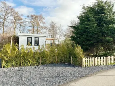 a small white house with a fence and trees at Chalet 552 op Recreatiepark De Wielen in Sint Maarten