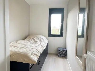 a small bedroom with a bed and a window at Chalet 552 op Recreatiepark De Wielen in Sint Maarten