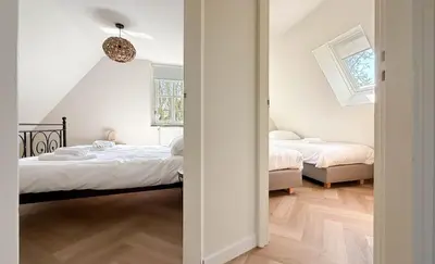 two beds in a room with white walls and wood floors at Zon aan den Hoef by Droomvilla in Egmond aan den Hoef