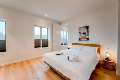 a white bedroom with a large bed with two windows at Villa Beachhouse in Bergen aan Zee
