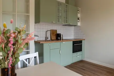 a kitchen with green cabinets and a table with a vase of flowers at Maria's hoeve Abcoude huisje 2 dichtbij Amsterdam in Abcoude