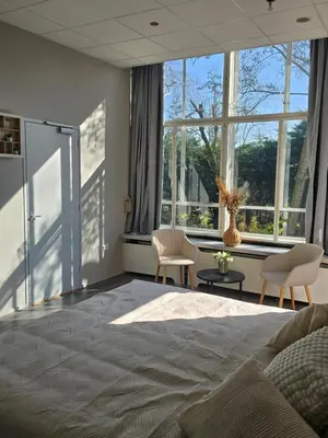 a bedroom with a bed and two chairs and windows at Hart van Warder in Warder