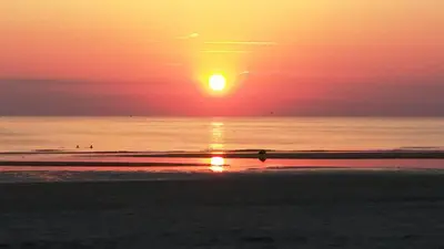 a sunset over the ocean with a person walking on the beach at Duinen Paradijs Zandvoort in Zandvoort