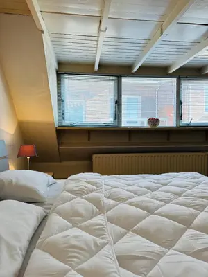 a large white bed in a room with windows at Strandhuisje Quarles in Noordwijk