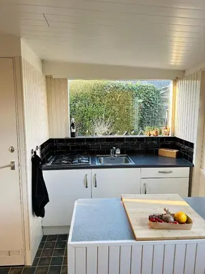 a kitchen with a sink and a counter with a cutting board at Beleef Noordwijk strandhuisje in Noordwijk aan Zee