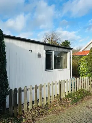 a white building with a fence next to it at Beleef Noordwijk strandhuisje in Noordwijk aan Zee