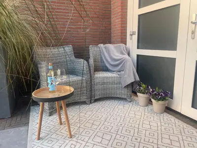 a patio with a chair and a table with a bottle of wine at Zon & blij in Katwijk aan Zee