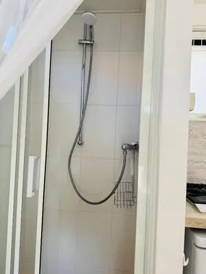 a shower in a bathroom with white tiles at Zeeschelpje in Noordwijk aan Zee