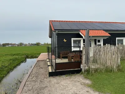 a black house with a wooden deck and a fence at BB Saari in De Woude