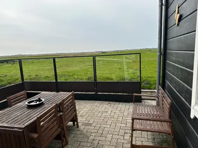 a patio with a table and chairs and a view of a field at BB Saari in De Woude