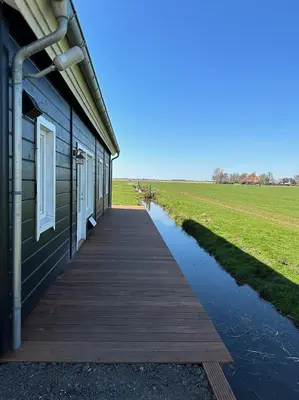 a wooden walkway next to a building next to a field at BB Saari in De Woude