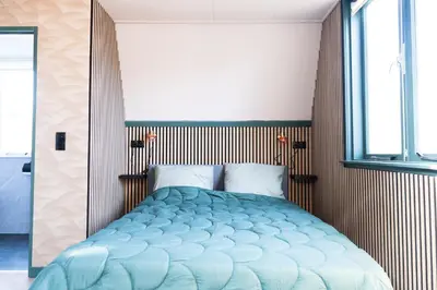 a bedroom with a blue bed with a window at 1 aan Strand in Egmond aan Zee