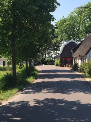 a tree lined road with a red barn and trees at De Vink Bed & Breakfast in Abcoude