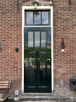 a black door in a brick building with a window at Het Koetshuis in Gouda