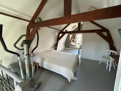 a bedroom with a white bed and wooden beams at Het Koetshuis in Gouda