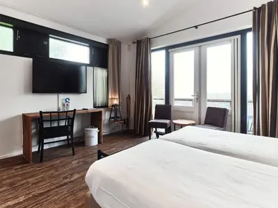 a hotel room with a bed and a desk and windows at Hajé Restaurant de Aalscholver in Lelystad