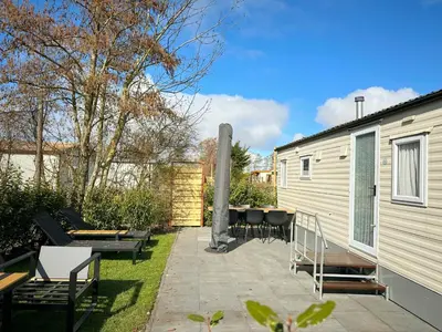 a patio with chairs and tables next to a trailer at Chalet 588 op Recreatiepark De Wielen in Sint Maarten