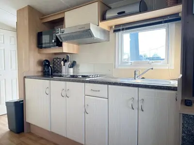 a kitchen with white cabinets and a sink and a window at Chalet 588 op Recreatiepark De Wielen in Sint Maarten