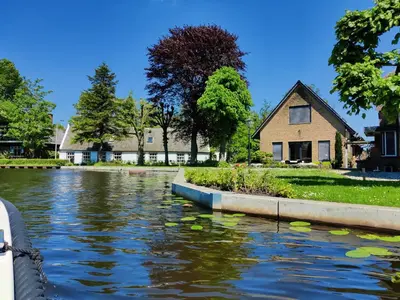 a house next to a river with leaves in the water at Park De Driesprong in Nieuwveen