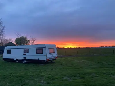 a white caravan parked in a field at sunset at De Rozenbottel met privé sanitair in Hensbroek