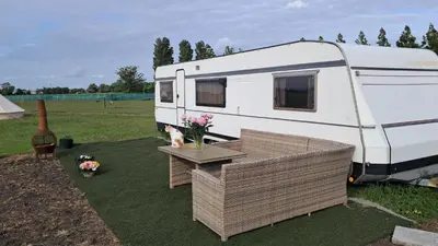 an rv parked in a field with a table and flowers at De Rozenbottel met privé sanitair in Hensbroek