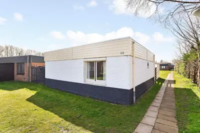 a white and black house in a yard at 4 person Bungalow at beach, sea, dunes, lake, forestside in Noordwijkerhout